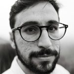 Close-up black and white portrait of a young man wearing eyeglasses, looking at camera.